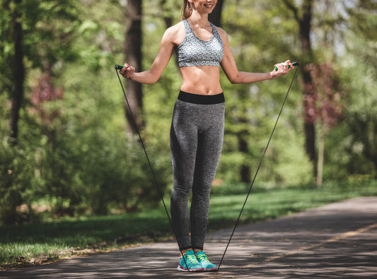 There is a woman in grey workout clothes and blue sneakers getting ready to jump rope on a bike path in nature.