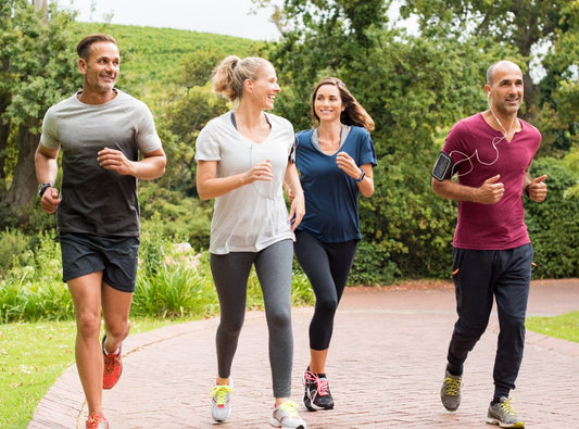 There is a group of four runners on a road with greenery behind them. There are two men and two woman wearing workout clothes and sneakers.
