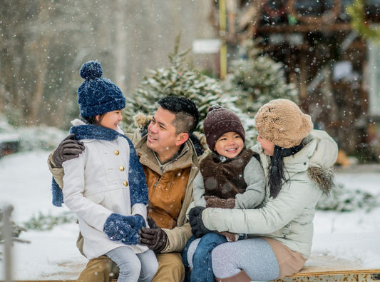 A family is sitting outside in the snow. They are wearing coats and there is a Mom, Dad, daughter and son.